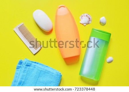 Flat lay bathroom items. Blue terry towel, wooden comb, soap, orange shampoo bottle, hair balm and seashells on a yellow background. Flat lay beauty photography, top view. Toiletries kit