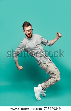 Handsome young stylish bearded man in glasses dancing in studio. Isolated on green background.