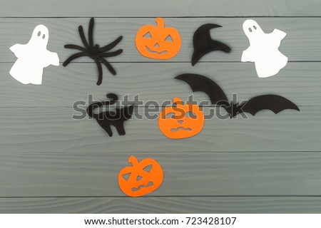 Halloween holiday background with three pumpkins, cat, spider, bat, hat and two ghosts cut paper on gray board