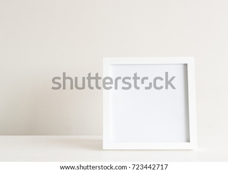 Square white blank picture frame on shelf against neutral wall background
