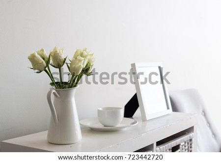 White roses in jug on shelf with cup and saucer and picture frame (selective focus)