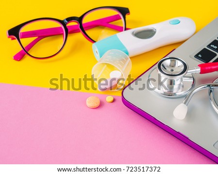 A medical stethoscope, thermometer, medicines and a laptop on a pink and yellow background. Health care and education concept.