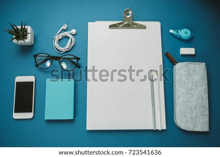 Space for work: a sheet of paper, pencils, phone, glasses, headphones on a blue background.