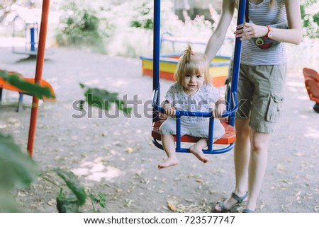 Baby girl swinging with her mother on the playground