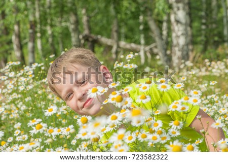 Happy boy playing in the field with flowers chamomile