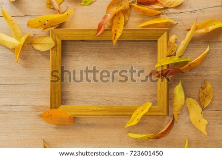 Golden wooden photo frame on wooden board with autumn leaves.