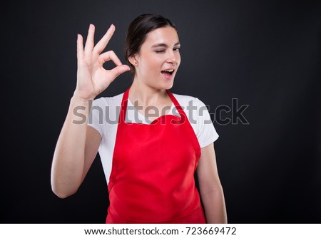 Young attractive woman in red apron posing happy and smiling giving okay hand sign