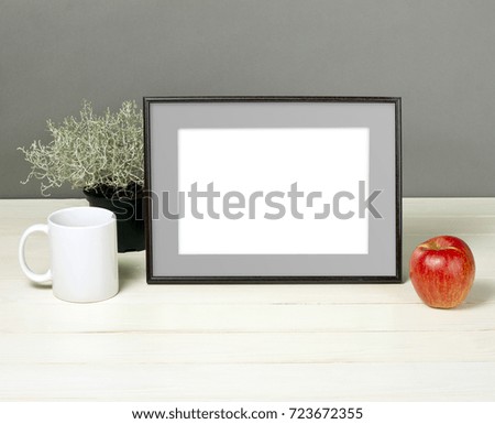 Frame mockup with plant pot, mug and apple on wooden shelf. Empty frame mock up for presentation design. Template framing for modern art.