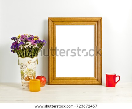 Brown frame mockup with field flowers in vase, apple, mug and candle. Empty frame mock up for presentation design. Template framing for modern art.