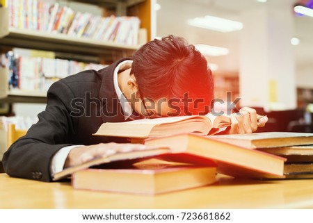 Advertising, Education,Business Concept -Sick and Tired. Exhausted businessman sleeping on piles of books and background blur bookshelf in library. Lens blur effect, Select focus (vintage color tone)
