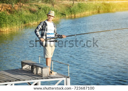 Young man fishing from pier on river