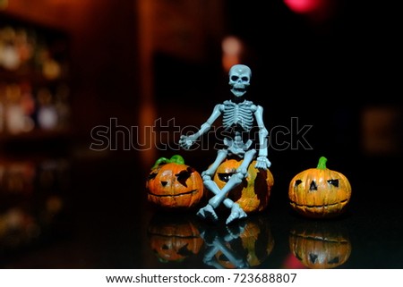skeleton plastic toy sit on pumpkin in dark background that mean halloween is coming