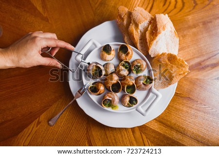 The above view of the person`s hand taking the snail shells full of the black caviar at the background of the wooden table.