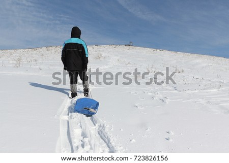 Man in a black jacket climbing a mountain with a plastic sled in winter, Russia, Bugotak Hills