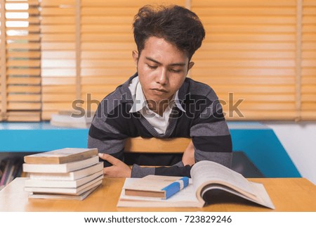 Advertising, Education Concept - Tired and stressed asian student in library.  (lens blur effect, select focus)