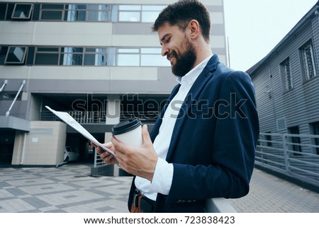 business man with a beard smiling in his hand papers and a glass of coffee on a building background                               