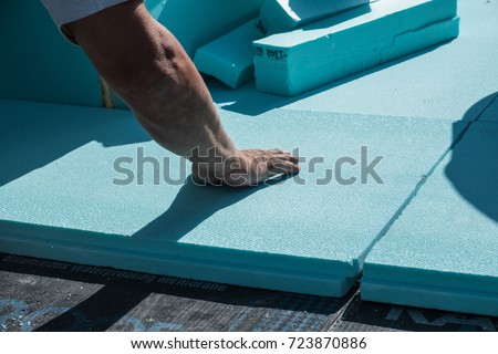 Worker placing XPS polystyrene insulation boards on the flat roof. Energy saving conceptual background. Royalty-Free Stock Photo #723870886