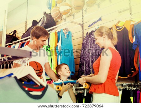 Cheerful smiling young parents giving skateboard to their son in school age in sport store
