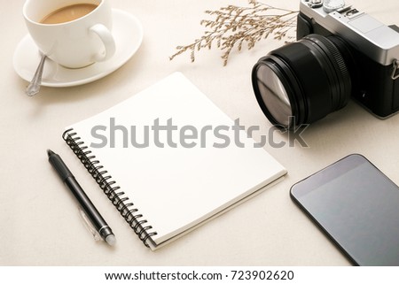 Blank notebook with cup coffee,Phone,Camera on white fabric,Top view with copy space.