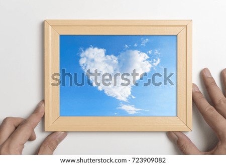 Hands holding picture frame with cloud heart