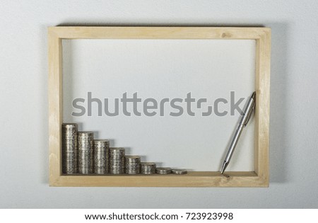 stack coin with pen in wooden frame on white wall background. Financial and saving concept.
