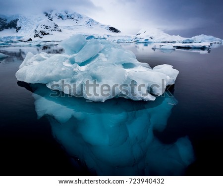 Small ice berg in clear, calm water showing turquoise ice underwater