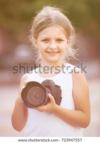 portrait of smiling caucasian girl in elementary school age holding photo camera in hands 