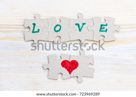 Word Love and heart made of pieces of jigsaw puzzle on light wooden table, close-up