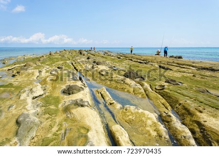 Rocky beach seaside landscape during good weather blue sky with unrecognized people fishing. A good picture for good weather and relax atmosphere.