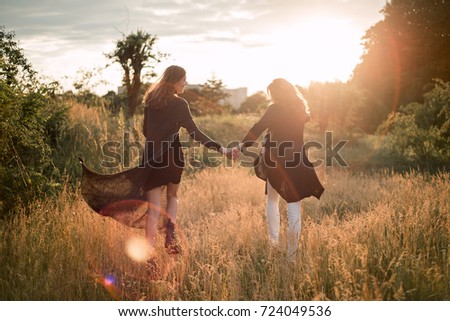 Mother and daughter photographed holding hands on the background of the sun and the sky