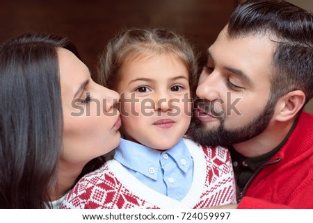 close-up portrait of happy parents kissing adorable little daughter looking at camera