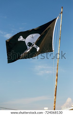 A flag evolving in the wind, depicting the skull as a symbol of pirates. Merry Roger / Skull and crossbones. Pirate flag against blue sky