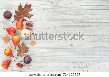 Abstract composition of fresh ripe organic pears, figs and dry leaves on a white wooden background. Pattern of fruits and leaves. Autumn harvest concept. Top view with free space for text.