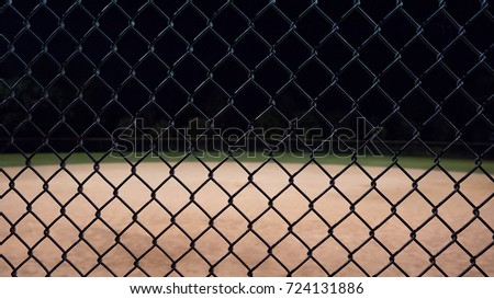 Looking through a baseball fence up close and seeing the field in the background.