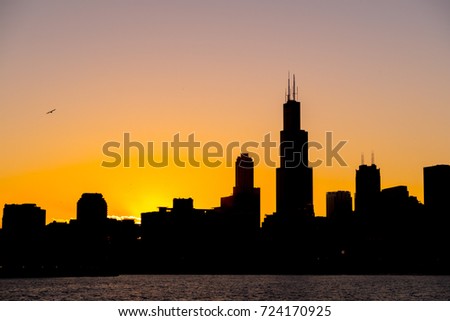 Chicago skyline picture during beautiful orange yellow sun as it lowers below the building silhouettes and the water of lake Michigan  in the foreground