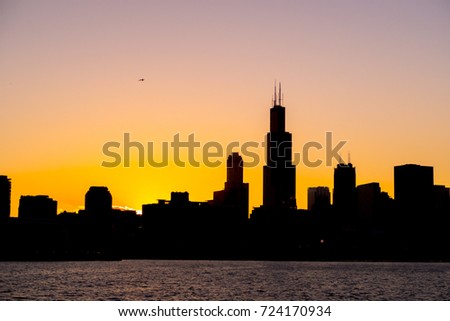 Chicago skyline picture during beautiful orange yellow sun as it lowers below the building silhouettes and the water of lake Michigan in the foreground