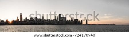 Chicago skyline panorama picture during beautiful sunset with building silhouettes and rippling waves of Lake Michigan water in the foreground
