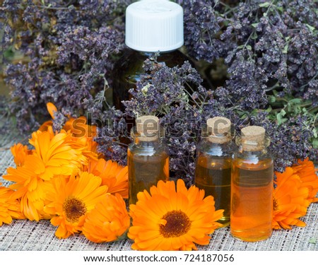three small vials and one big bottle with calendula tincture on a table with dtied herbs behind