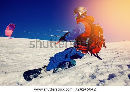 Snowboarder with a kite on fresh snow in the winter in the tundra against a clear blue sky. Teriberka, Kola Peninsula, Russia. Concept sports snowkite. Royalty-Free Stock Photo #724246042