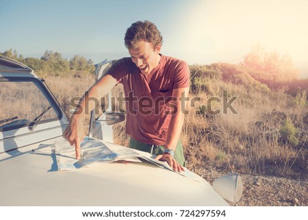 Vintage style image of a man looking at a map over a car in countryside.