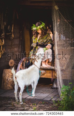 Funny picture a beautiful young girl farmer with a wreath on her head with white goat.