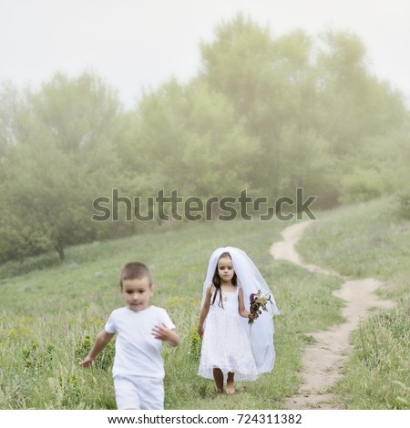 Young bride and groom playing wedding summer outdoor. Children like newlyweds. Little groom is running away from his young bride, funny kids game. Bridal, wedding concept, image toned and noise added.