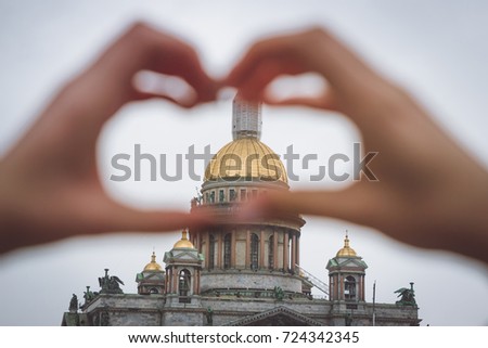 Symbol of heart made up of fingers of girls through it is seen St. Isaac's Cathedral in St. Petersburg on cloudy day shallow depth of field