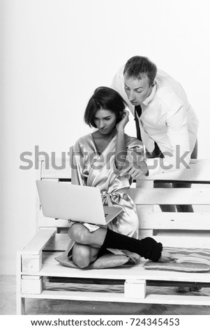 young couple of handsome man or businessman and pretty woman or girl working on portable laptop or computer in shirt, socks and tie, sits on wooden bench at home isolated on white background