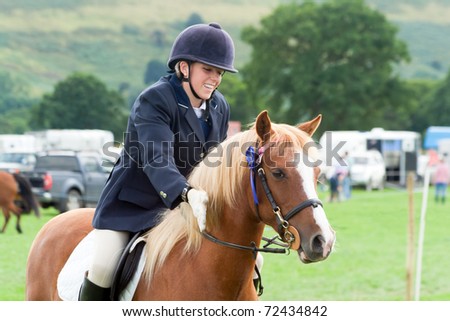 Pretty girl patting her pony in congratulations after winning a rosette for show jumping. Royalty-Free Stock Photo #72434842