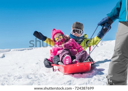 Father sledding his little son and daughter. Cute girl and happy boy being pulled on a red sled. Dad pulling his children in a bobsled on the snow. Winter vacation with family on snowy mountains.