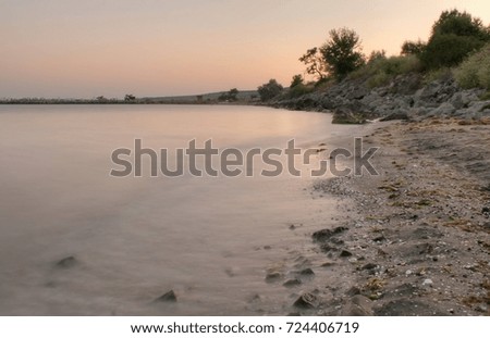 Beautiful seascape. Rocks in the water, blurred waves and flat sea water surface. Pink light at sunset time.