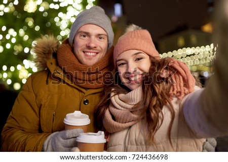 winter holidays, hot drinks and people concept - happy couple with coffee taking selfie in christmas evening