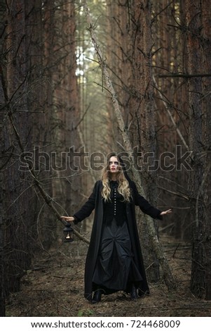 Halloween. beautiful girl with a lantern in a black dress in the forest