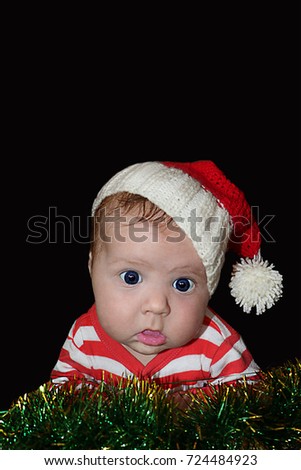 Newborn baby in santa hat with dumbfounded face looking at camera isolated on black background.  for design of banners, flyers, calendars, invitations  as clip art. Place for text.